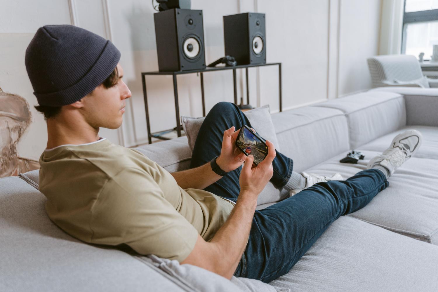 Hombre relajado en el sofá jugando con su teléfono Android, simulando una consola portátil