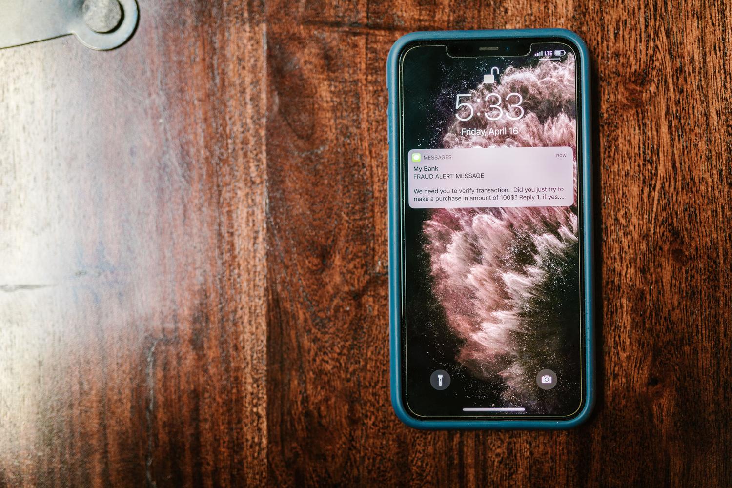 Primer plano de un smartphone sobre una mesa de madera mostrando un mensaje de alerta de fraude en la pantalla, señal de advertencia para el usuario.