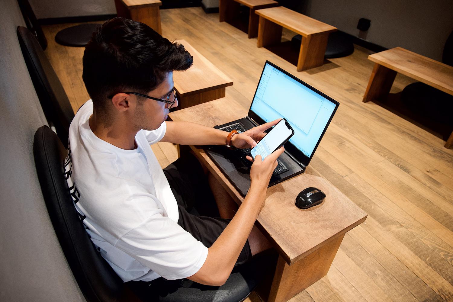Hombre utilizando simultáneamente un portátil y un móvil, destacando la fluidez de la navegación al tener la cuenta vinculada.
